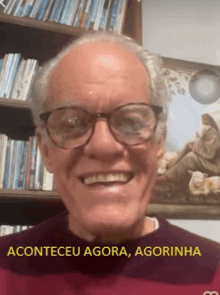 a man wearing glasses is smiling in front of a bookshelf with the words aconteceu agora agorinha