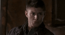 a man in a black jacket is sitting in a dark room and looking at the camera .