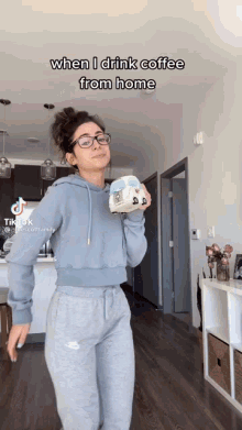 a woman in a blue hoodie and grey sweatpants is holding a cup of coffee in her hand ..