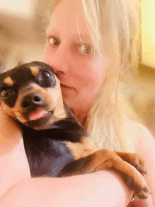 a woman is holding a small black and brown dog in her arms