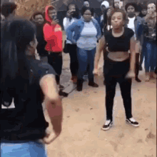 two women are standing next to each other in front of a crowd of people on a dirt road .