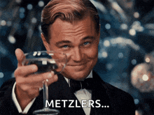 a man in a tuxedo is holding a glass of wine and the word metzlers is next to him