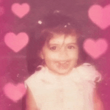 a little girl is smiling in front of a background of pink hearts .