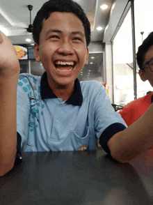 a boy wearing a blue shirt with a black collar is smiling