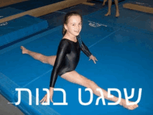 a girl in a black leotard is doing a split on a blue mat in hebrew