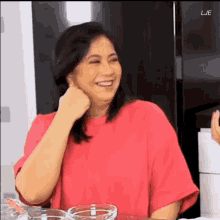 a woman in a pink shirt is smiling and laughing while sitting at a table with a bowl of water .