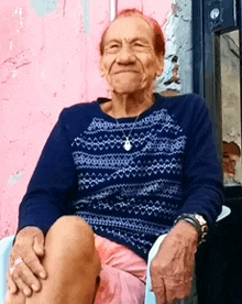 an elderly woman wearing a blue sweater sits in a chair with her legs crossed