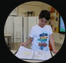 a young boy in a white shirt is looking at a book in a classroom .