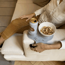 a woman sits on a couch with a bowl of nuts and a can of beer