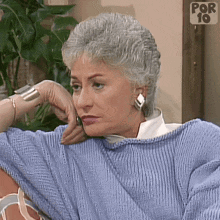 a woman wearing a blue sweater and earrings is sitting on a couch .