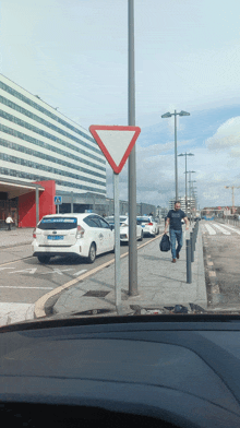 a man walking down a sidewalk next to a white car that says taxi