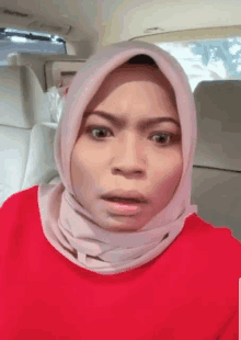 a woman wearing a hijab and a red shirt is making a funny face