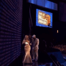 a woman stands on a stage in front of an american music awards screen