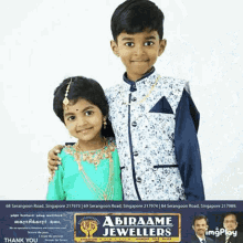 a boy and a girl are posing for a picture in front of a sign that says abirame jeweller 's