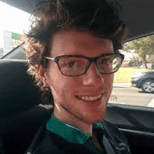 a man wearing glasses is sitting in the back seat of a car .