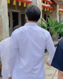 a man in a white shirt is standing in front of a building with chinese lanterns hanging from the ceiling .