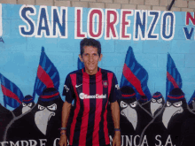 a man in a san lorenzo jersey stands in front of a mural