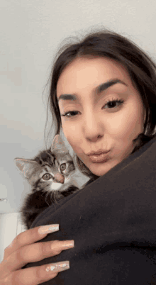 a woman holds a kitten in her arms and looks at the camera