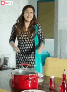 a woman in a black and white dress is standing in front of a table with a red pot on it .