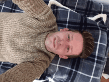 a man wearing a brown sweater is laying on a plaid blanket