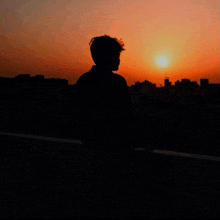 a silhouette of a man standing in front of a city at sunset