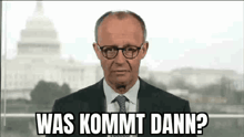 a man in a suit and tie is standing in front of a microphone and says `` was kommt dann ? '' .