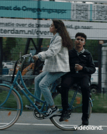 a man and a woman are riding a bike in front of a sign that says " met de omgevingsapp "