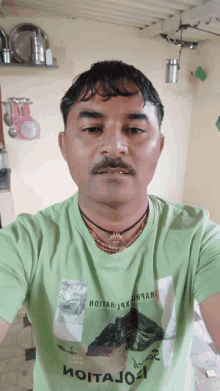 a man wearing a green t-shirt with a picture of a mountain on it poses for a picture