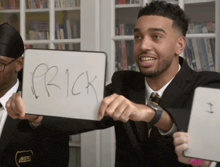 a man in a suit is holding up a white board with the word prick written on it