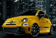 a yellow abarth car is parked in front of a city skyline at night