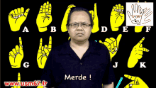 a man with glasses says merde in front of the alphabet