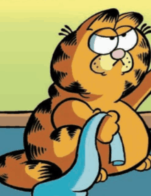 garfield the cat is holding a blue towel in his paws while sitting on the floor .