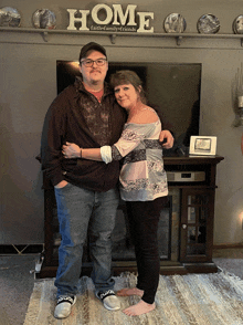 a man and a woman are posing in front of a sign that says home