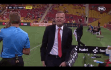 a man in a suit and tie stands on a soccer field with a fox sports logo on the bottom