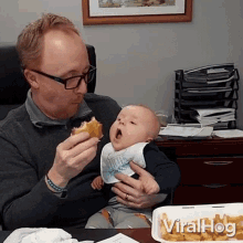 a man is holding a baby while eating a sandwich and the baby is wearing a bib that says " little prince "