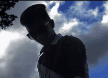 a silhouette of a man wearing sunglasses against a cloudy sky .