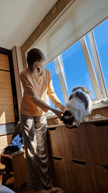 a woman playing with a cat in front of a large window