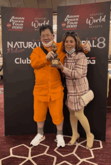 a man holding a trophy stands next to a woman in front of a sign that says asian poker tour 2022