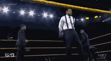 a man in a suit and suspenders stands in a wrestling ring with a usa logo in the corner