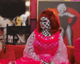 a woman with a checkered face is sitting on a couch in front of a picture of marilyn monroe