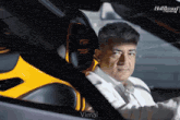 a man in a white shirt is sitting in a car with the hollywood reporter behind him