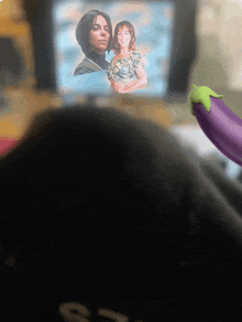 a picture of a man and a woman is displayed on a screen next to an eggplant