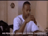 a man in a white shirt is sitting at a table with his hands folded and says `` come get these cardinals ! ''