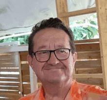 a man wearing glasses and an orange shirt is smiling for a picture .