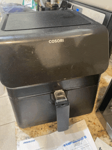 a cosori air fryer sits on a counter next to a progressive envelope