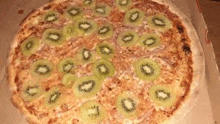 a pizza with kiwi slices on top is in a box .