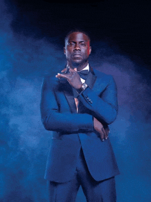 a man in a blue suit and bow tie is standing with his hands folded