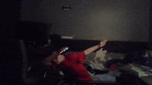 a man in a red shirt is dancing in a dark room with a batman sticker on the wall behind him