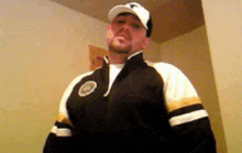 a man wearing a baseball cap and a jacket is standing in a hallway .