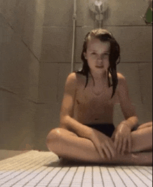 a shirtless young girl is sitting on the floor in a shower .